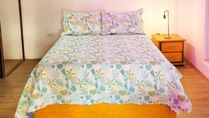 Un dormitorio con cama, mesita de noche, lámpara y un cuadro de una playa.