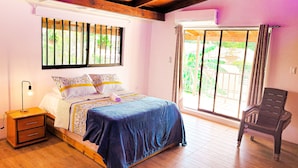 Un dormitorio con cama, mesita de noche, una silla y ventana con vistas al verdor.