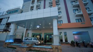 Ein mehrstöckiges Hotel mit moderner Fassade, großem Glas Eingang und einem überdachten Außenbereich mit Autos und Motorrädern.