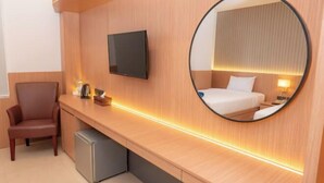 Ein Hotelzimmer mit Bett, Schreibtisch, Stuhl, Fernseher und Spiegel.