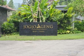 Letrero de Jogi Aeng con un exuberante jardín de fondo.