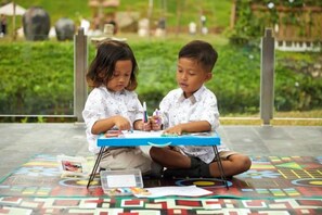 Two children sitting at a table outdoors with art supplies. - Joglo Ageng Guci Tegal (Bumijawa)