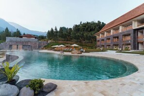 A pool area with lounge chairs and umbrellas, surrounded by a building with multiple balconies.
