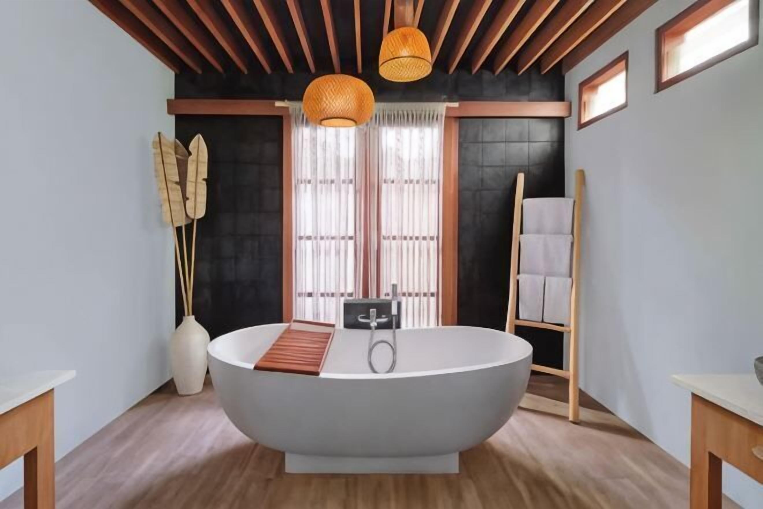 Un baño moderno con una bañera independiente, vigas de madera en el techo y un amplio ventanal con cortinas traslúcidas.
