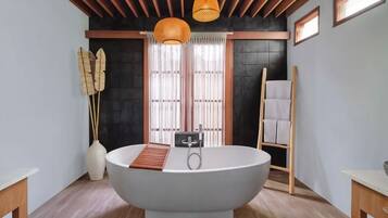 A modern bathroom with a freestanding bathtub, wooden ceiling beams, and a large window with sheer curtains.