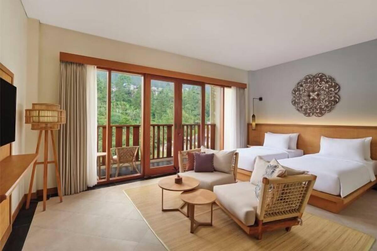 A hotel room with a large balcony, a sofa, a bed, a TV, and a decorative wall piece.