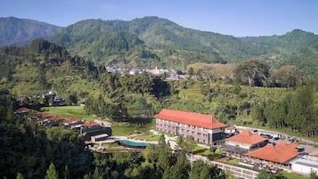 A hotel with a red roof, surrounded by lush greenery and mountains in the background.