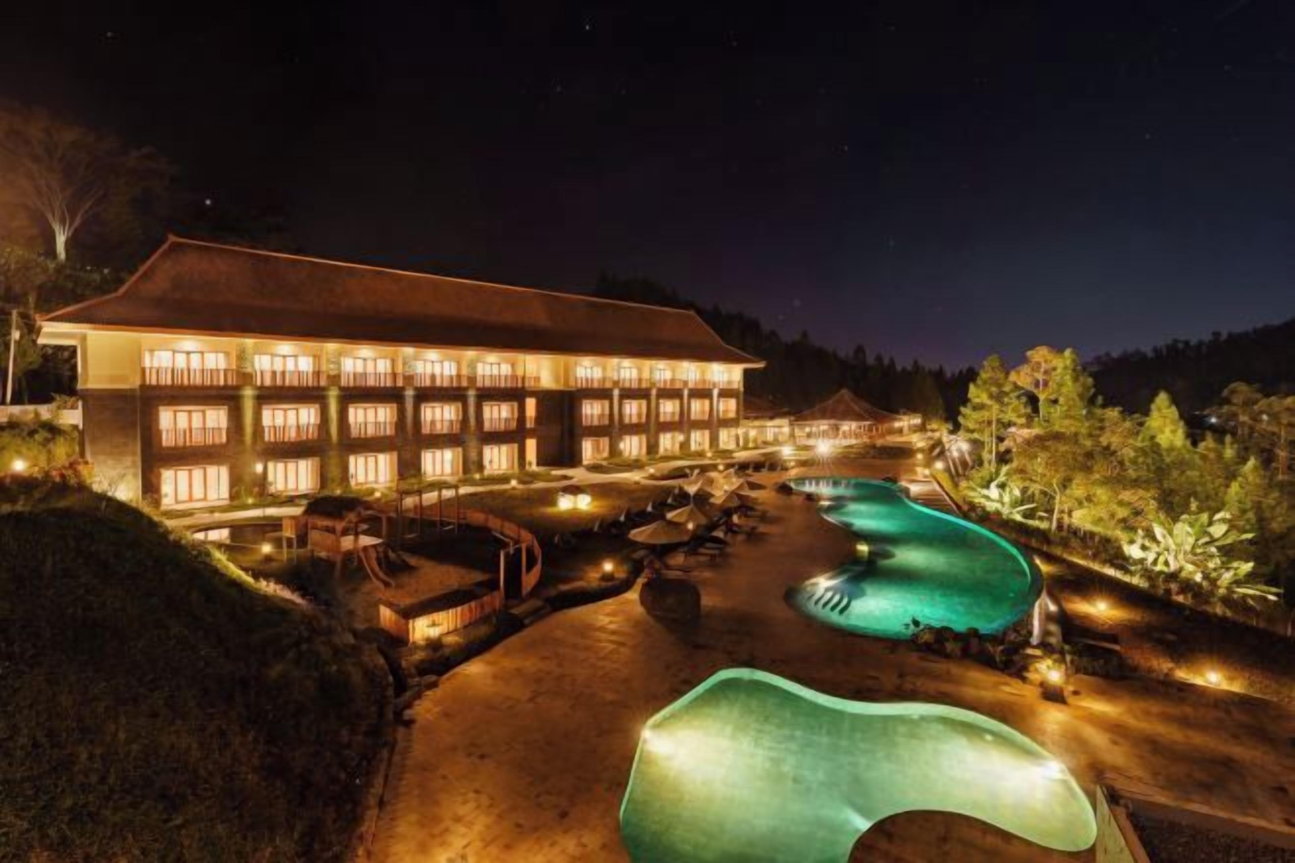 A hotel with a swimming pool and a well-lit exterior at night.