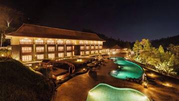 A hotel with a swimming pool and a well-lit exterior at night.