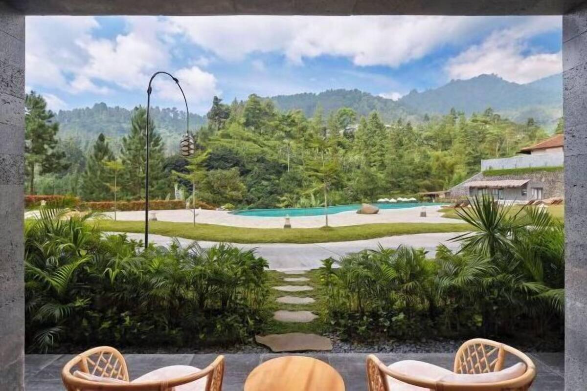 A view from a balcony overlooking a pool, lush greenery, and mountains.
