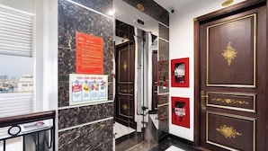 Een hotel lobby met marmeren wanden, een houten deur met gouden accenten en een rode brandblusser.
