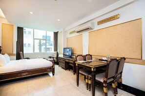A hotel room with a bed, a desk, a television, and a view of the city.