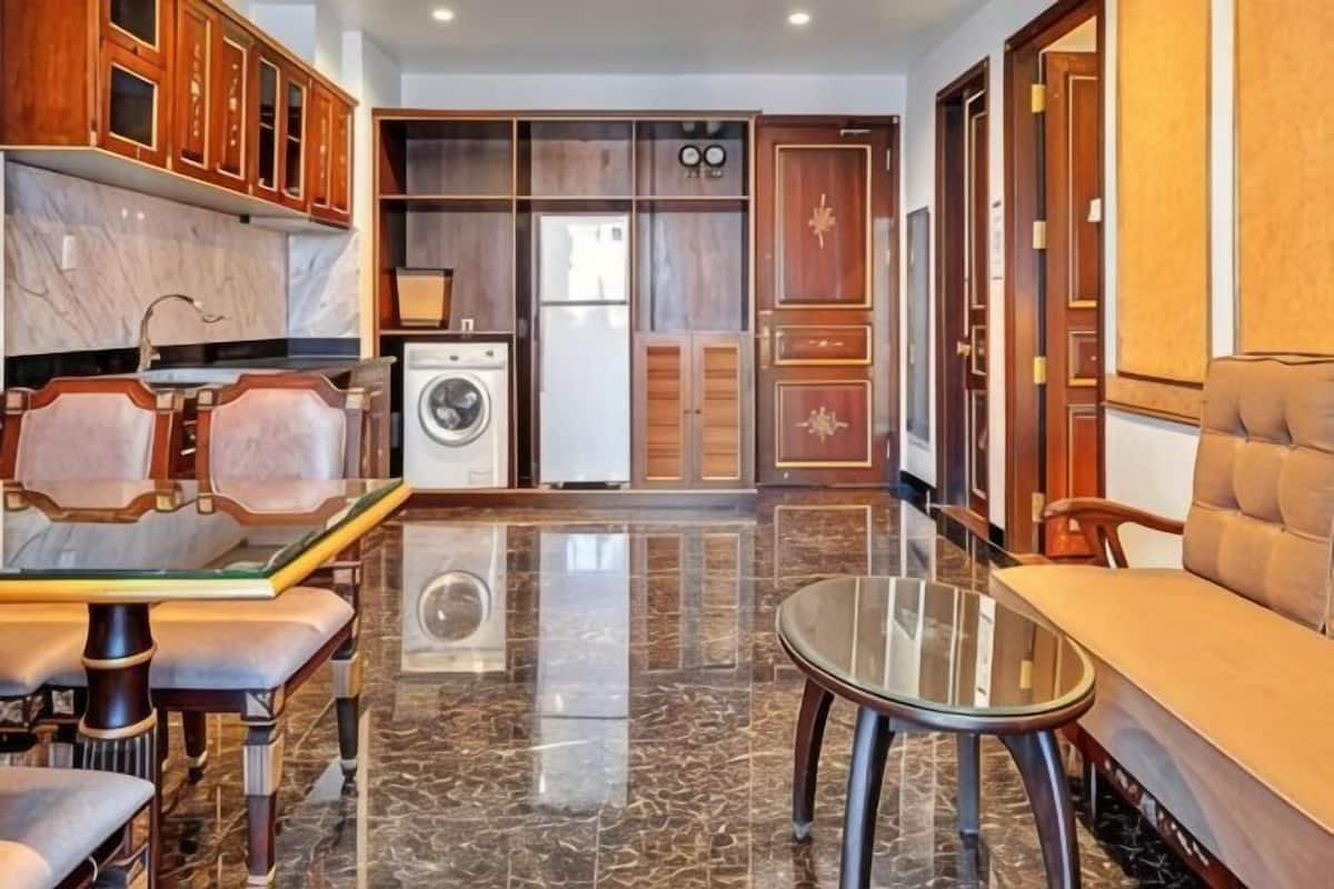 A modern kitchen with marble countertops, a glass-top dining table, wooden cabinets, and a built-in washer and dryer.