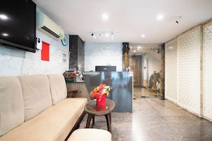 A hotel reception area with a reception desk, a sofa, and a small table with a vase of flowers.