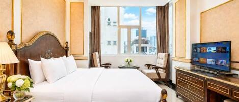 A hotel room with a large bed, a television, a desk, and a view of the city.