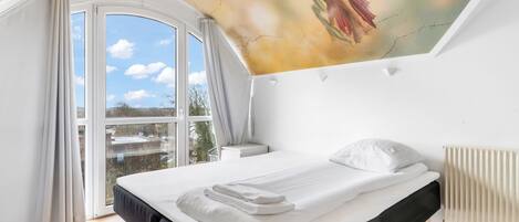 Un dormitorio con una cama grande, una ventana con cortinas, un radiador y un mural en el techo.