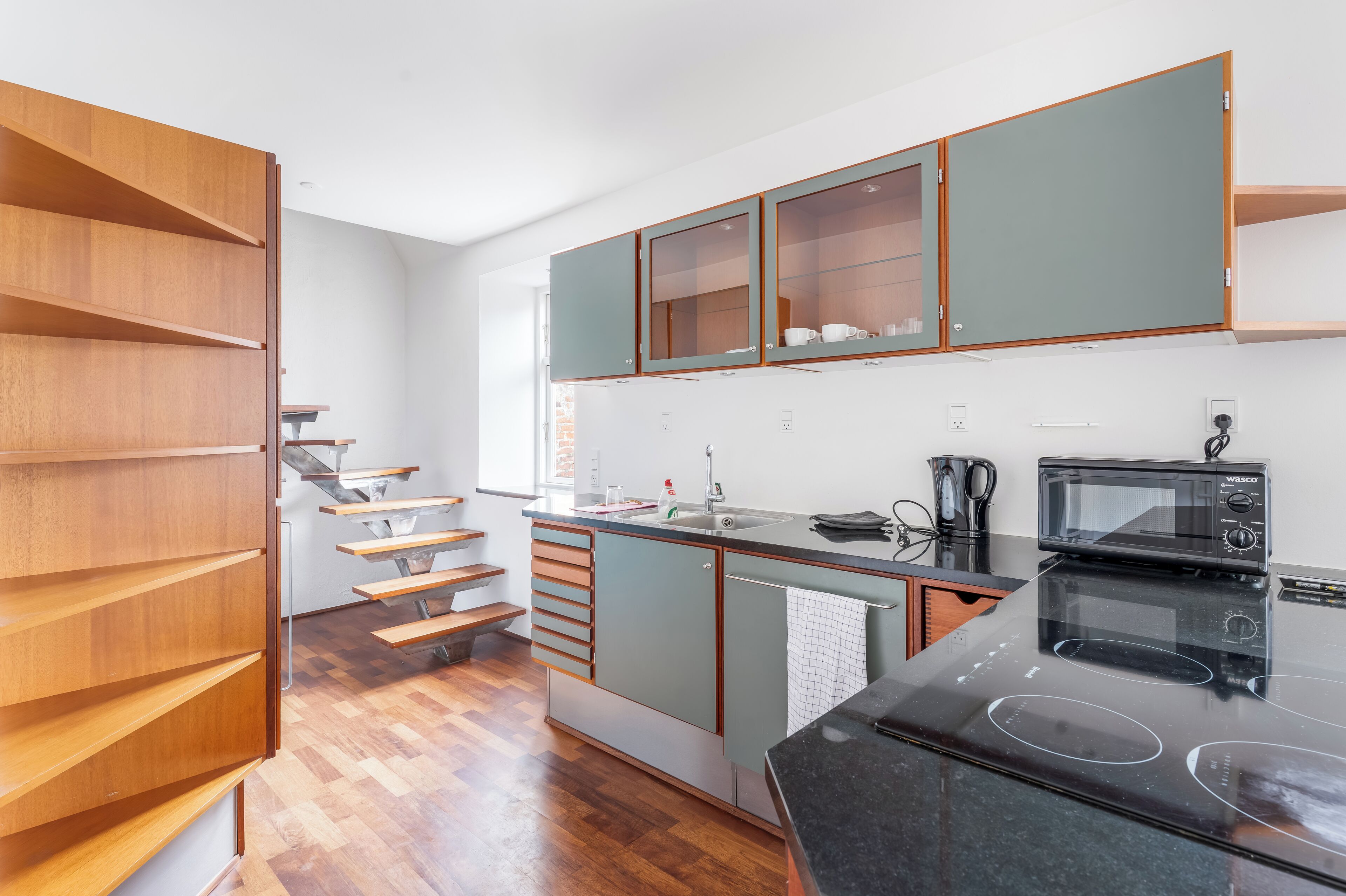 A modern kitchen with wooden shelves, a built-in stove, and a microwave.