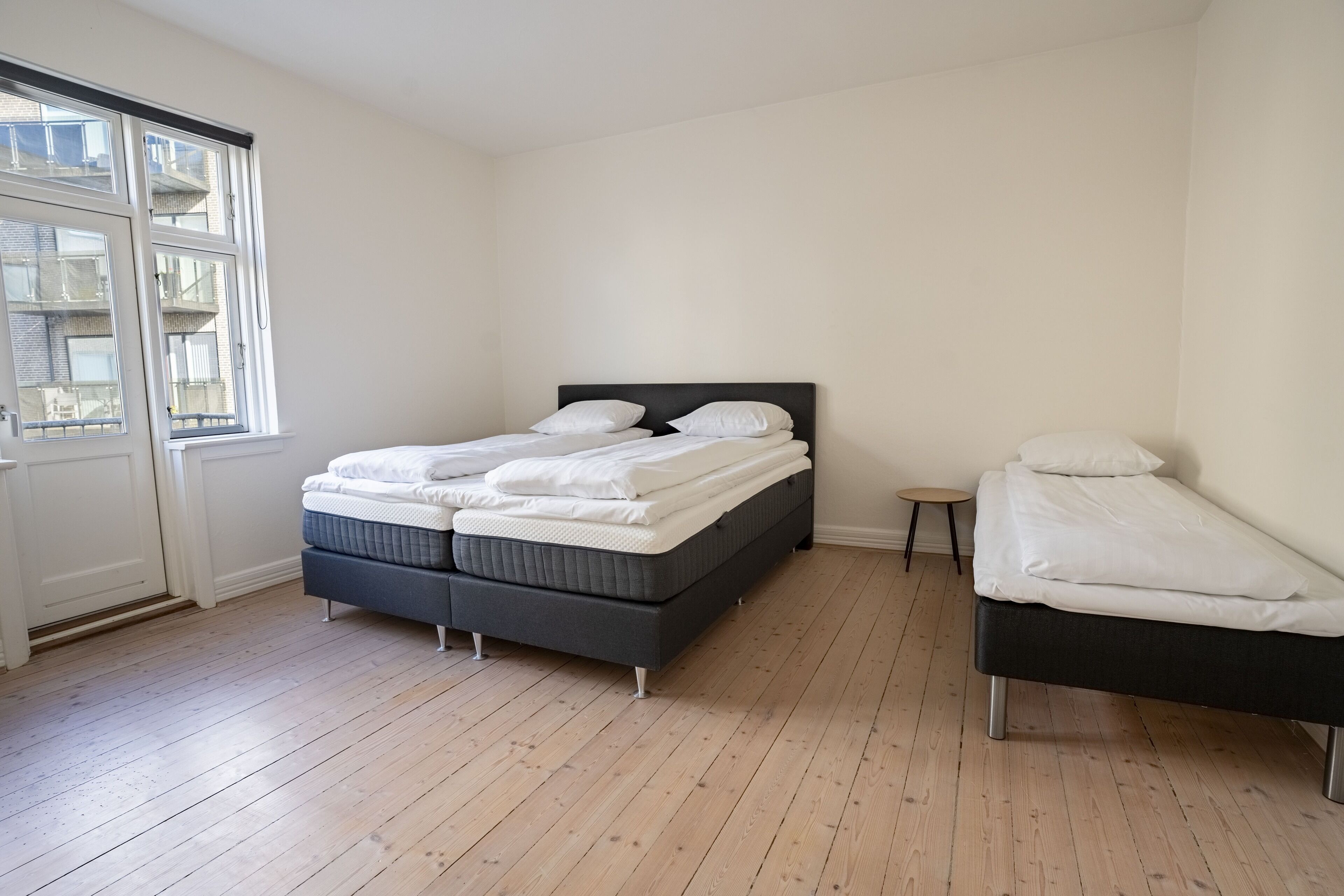 Un dormitorio con una cama doble, una cama individual y una mesita de noche pequeña.