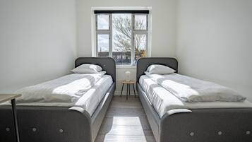 Un dormitorio con dos camas individuales, una mesita pequeña y una ventana con vistas a edificios y árboles.