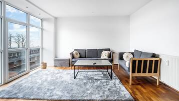 Una sala de estar moderna con un sofá gris, una mesa de centro de madera y una alfombra gris sobre piso de madera.