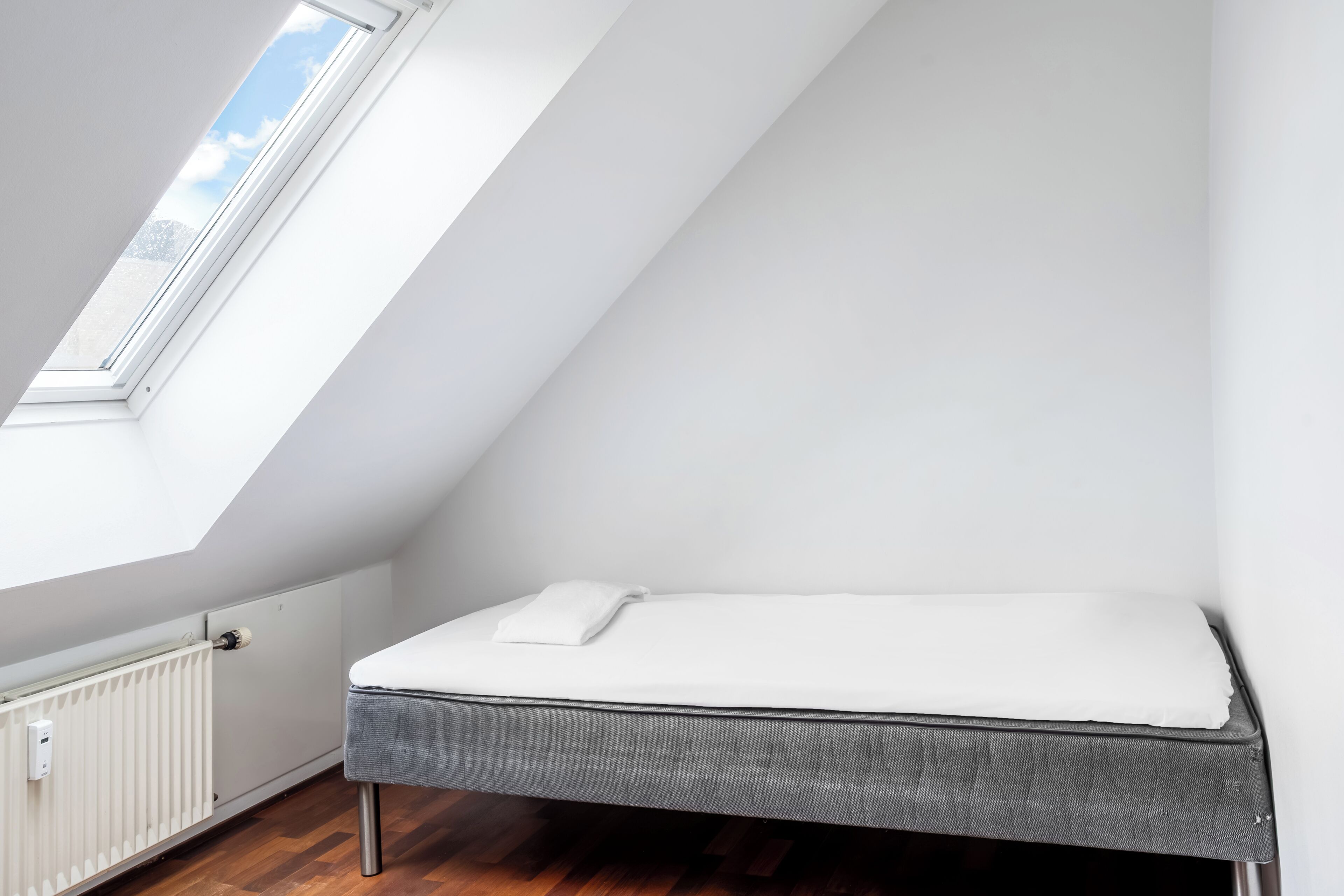 Une petite chambre avec un lit simple, un plafond en pente et une fenêtre laissant entrer la lumière naturelle.