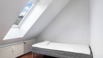 Une petite pièce aux murs inclinés, dotée d’un puits de lumière, d’un lit et d’un radiateur.