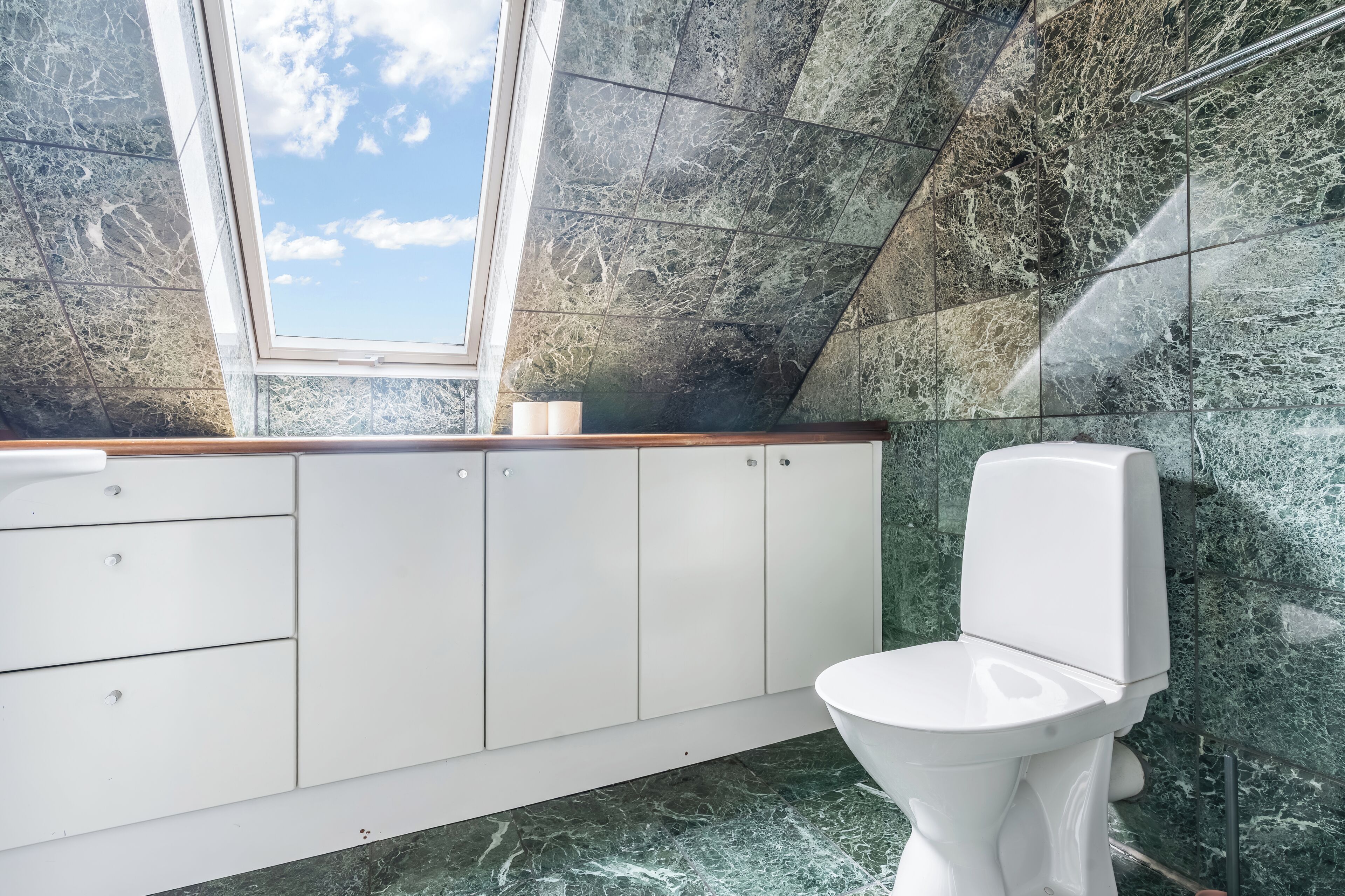 Un baño moderno con tragaluz, inodoro blanco y paredes de mármol.