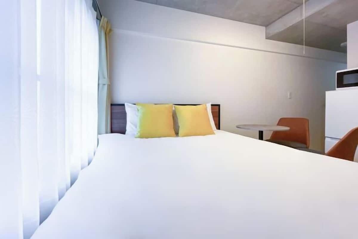 Una habitación de hotel con una cama, dos almohadas, una mesita y una silla.