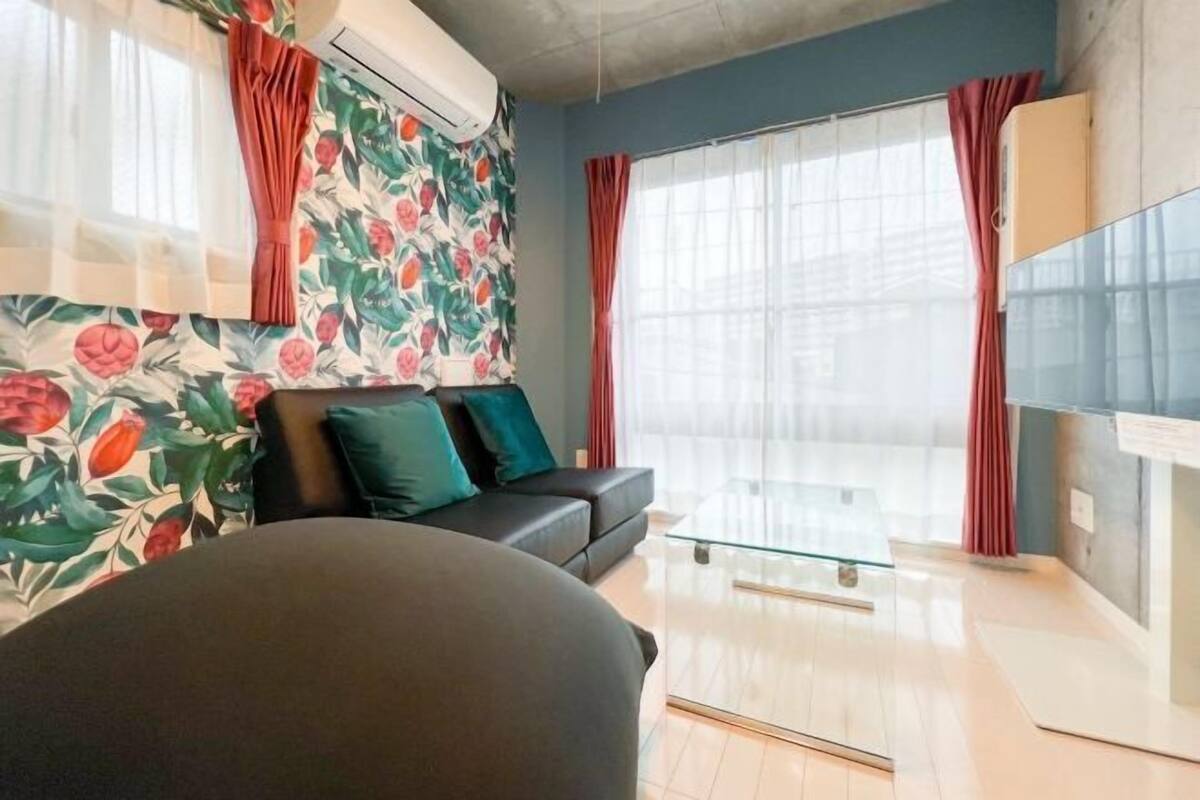 Una sala de estar moderna con sofá, una mesa de centro de vidrio y un ventanal con cortinas.