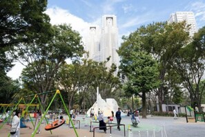 A park with playground equipment, trees, and tall buildings in the background. - ION Shibuya-honmachi (Tokyo)