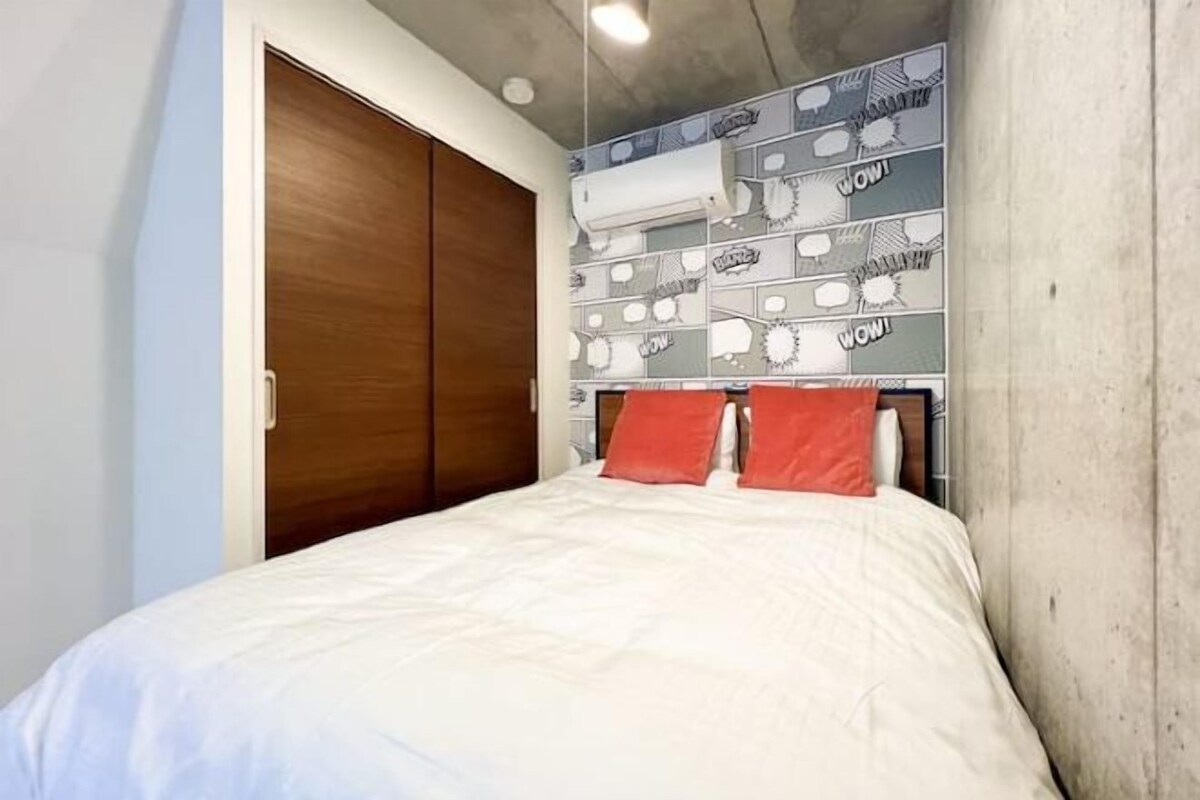 A bedroom with a bed, a wooden wardrobe, and a wall with comic book-style wallpaper.
