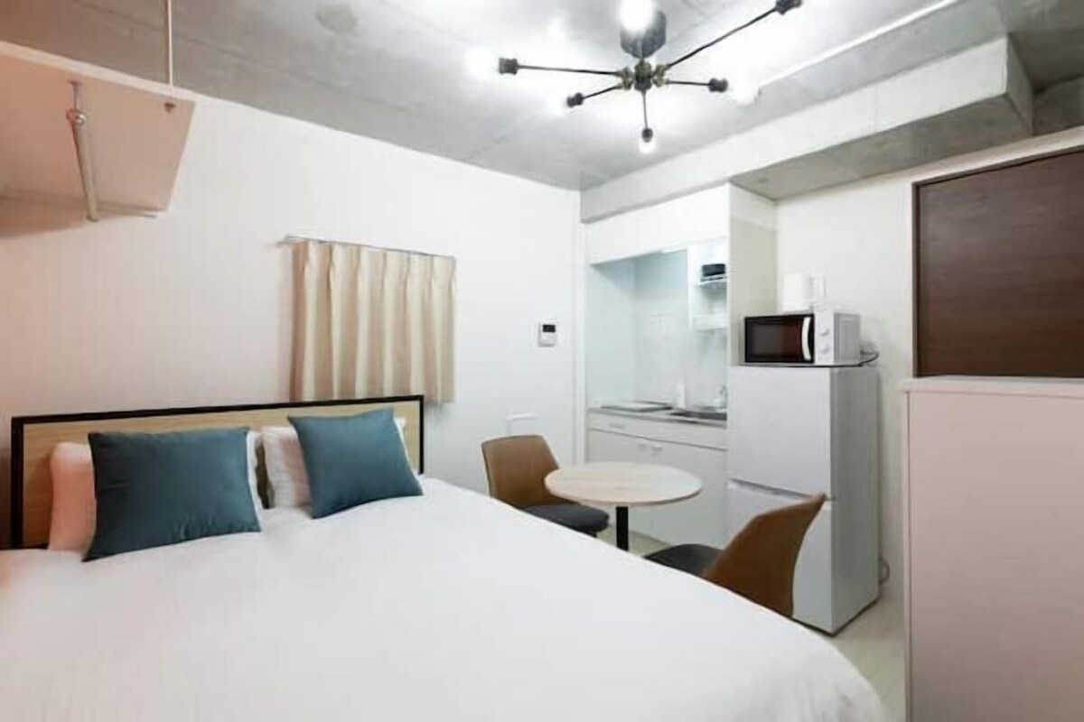 A hotel room with a bed, a small table, a chair, a microwave, and a kitchenette.