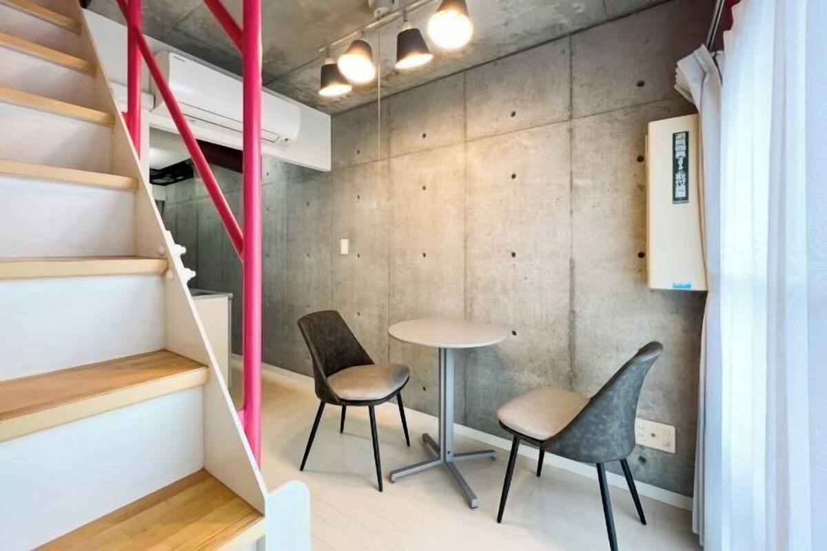 A modern interior with a staircase, two chairs, a small table, and a concrete wall.