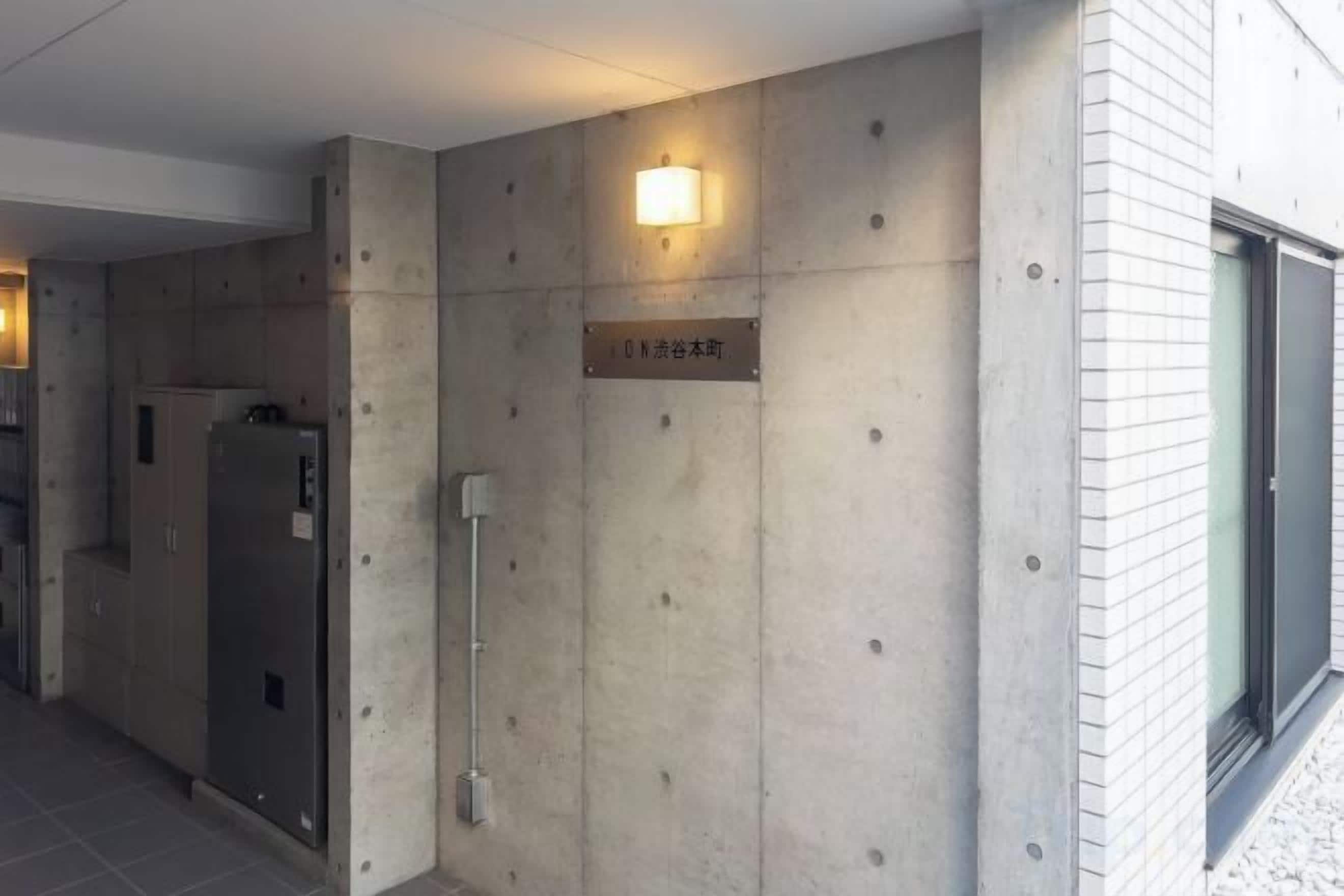 A hallway with a sign indicating a room number, a door, and a wall-mounted light fixture.