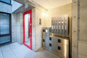 Un pasillo con una puerta roja, taquones metálicos y un accesorio de iluminación.