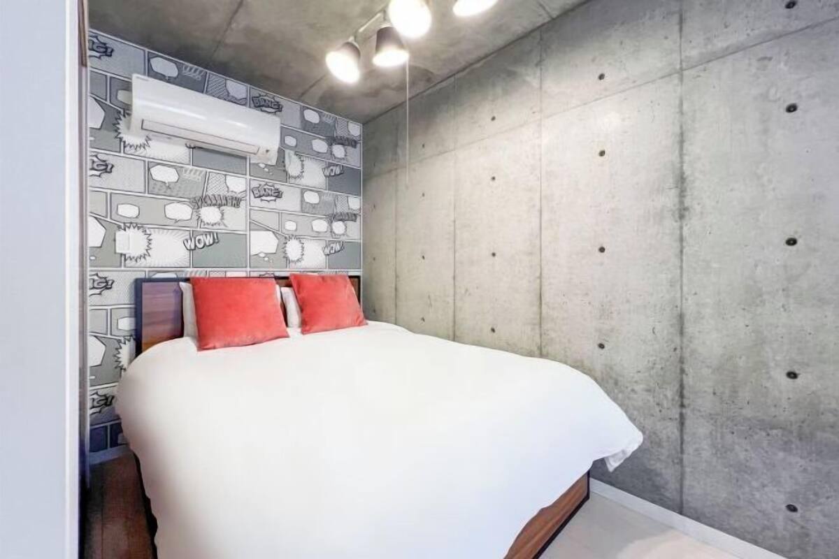 Un dormitorio con cama, cabecera de diseño estampado y pared de concreto.
