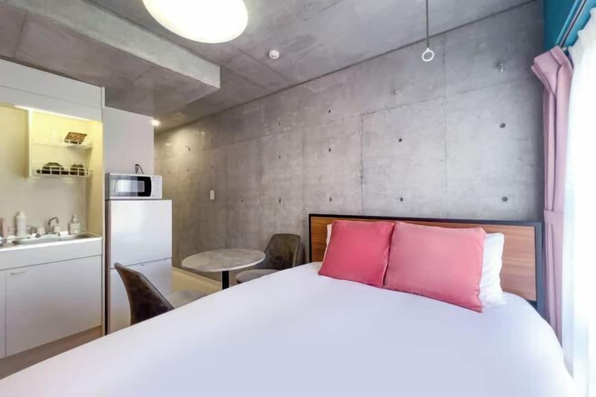 Una habitación de hotel con cama, kitchenette, mesa redonda y una silla.