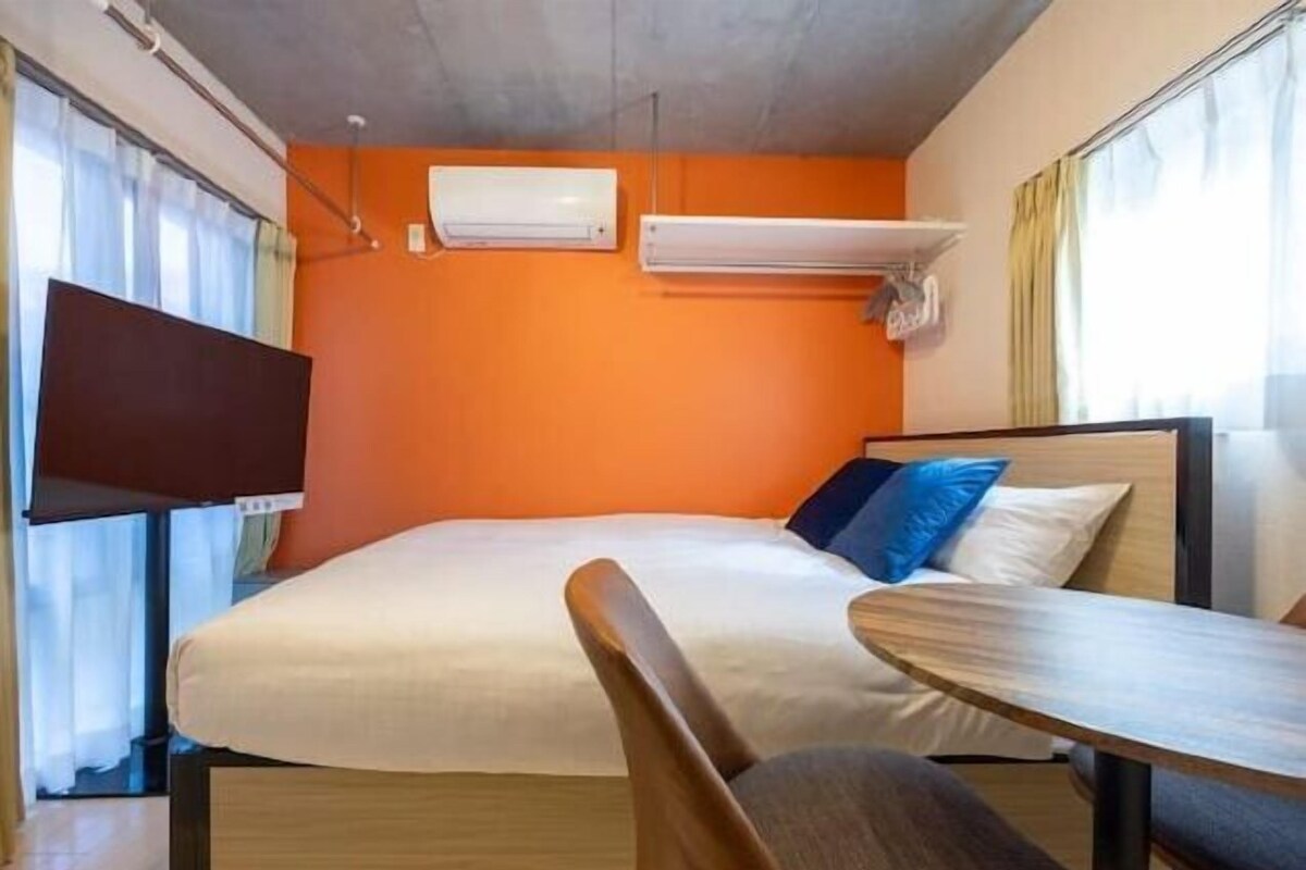 A hotel room with a bed, a TV, and two air conditioning units on the wall.
