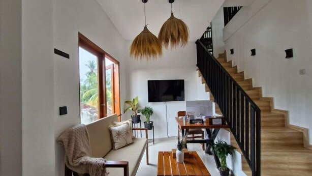 Ein großzügiger Wohnbereich mit Sofa, Couchtisch und Esstisch, einer Treppe sowie einem an der Wand montierten Fernseher.
