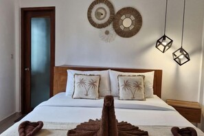 A hotel room with a bed, pillows with palm tree designs, wall art, and hanging geometric light fixtures. - Lemon Tree Hotel Bali (Bali)