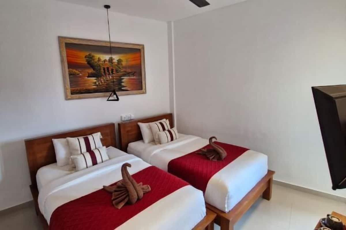 A hotel room with two beds, a painting on the wall, and a television on the right.