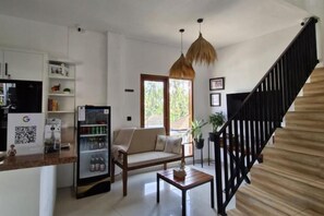 A living room with a sofa, a coffee table, a refrigerator, and a hanging light fixture. - Lemon Tree Hotel Bali (Bali)
