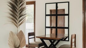 Un coin repas avec une table et des chaises en bois, une grande plante décorative et un miroir encadré de noir accroché au mur.