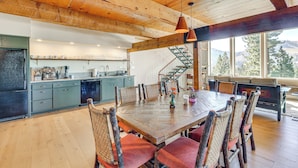 A spacious dining area with a large wooden table and wicker chairs, a kitchen with light blue cabinets, and a staircase leading to a loft. - Endless Mtn Views! Group Ski Lodge at Sugar Bowl (Norden)