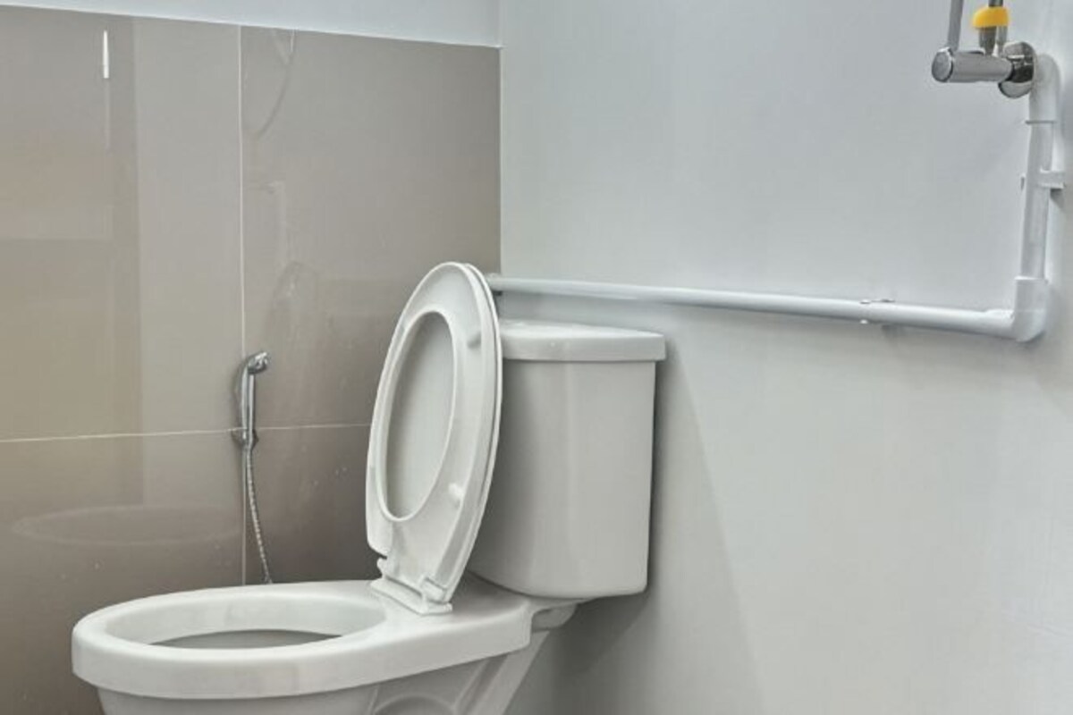 A toilet with a closed lid, a shower area, and a wall-mounted pipe.
