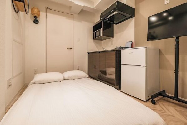 A bedroom with a bed, a white refrigerator, a microwave, and a television. - Shinjuku Yoyogi Hearts House (Tokyo)
