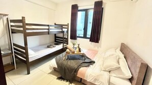 Een kamer met stapelbedden, een nachtkastje met een lamp, en een raam met gordijnen.