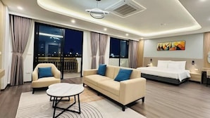 A modern hotel room with a sofa, a round coffee table, a bed, and a view of the city at night.