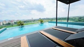 A rooftop infinity pool with lounge chairs and a wooden deck.