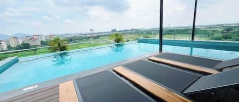 A rooftop infinity pool with lounge chairs and a wooden deck.